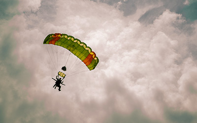 Instructor y aprendiz haciendo paracaidismo con el cielo nublado de fondo.