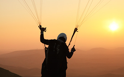 Persona regulando las cuerdas de su paracaidas listo para hacer parapente durante el atardecer en las montañas.